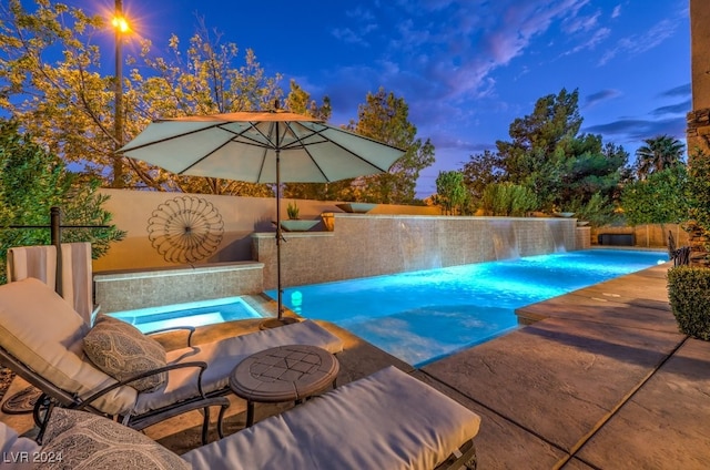 pool at dusk featuring an in ground hot tub and pool water feature