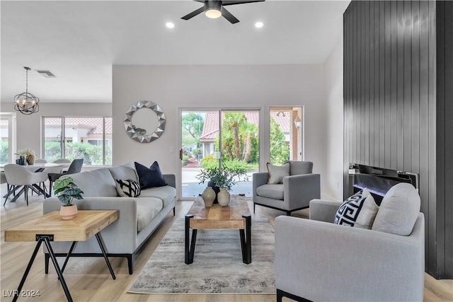 living room with ceiling fan with notable chandelier and light hardwood / wood-style floors