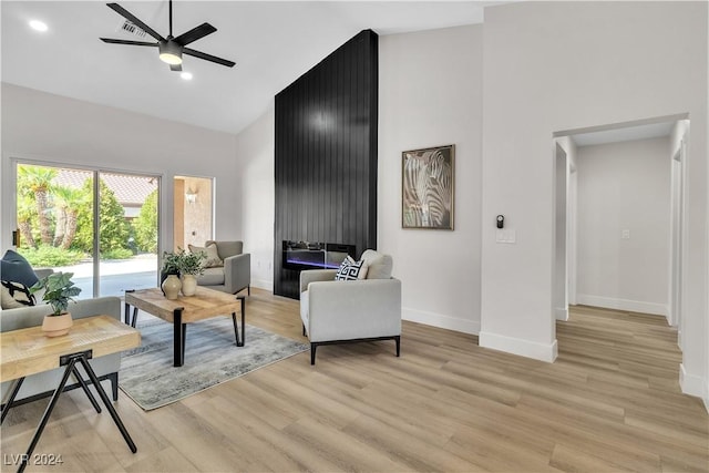 living room with ceiling fan, light wood-type flooring, and a towering ceiling