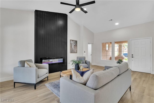 living room with ceiling fan, a large fireplace, vaulted ceiling, and light wood-type flooring