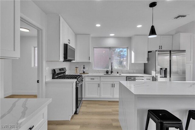 kitchen with light stone countertops, a breakfast bar, stainless steel appliances, light hardwood / wood-style flooring, and white cabinetry