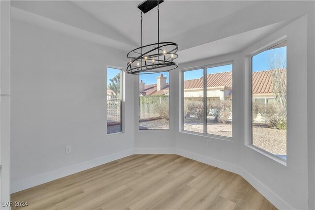 unfurnished dining area with lofted ceiling, light hardwood / wood-style floors, an inviting chandelier, and a healthy amount of sunlight