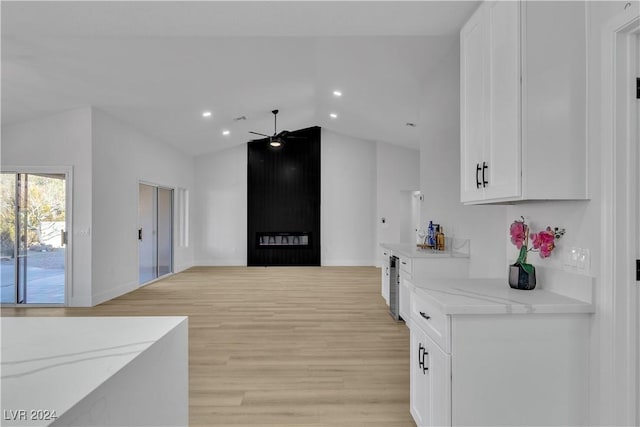 kitchen featuring ceiling fan, light stone counters, light hardwood / wood-style floors, vaulted ceiling, and white cabinets