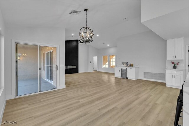 unfurnished living room with lofted ceiling, beverage cooler, a notable chandelier, and light wood-type flooring