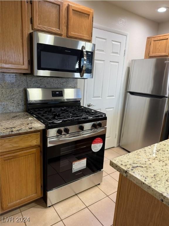 kitchen featuring light stone counters, light tile patterned floors, decorative backsplash, and stainless steel appliances