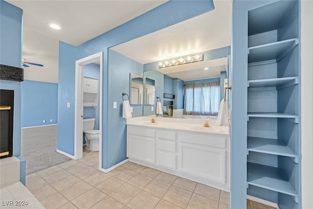 bathroom featuring a tiled fireplace, tile patterned floors, toilet, vanity, and ceiling fan