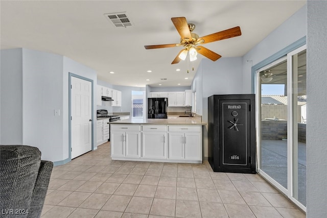 kitchen featuring light tile patterned flooring, black fridge, sink, white cabinets, and stainless steel range