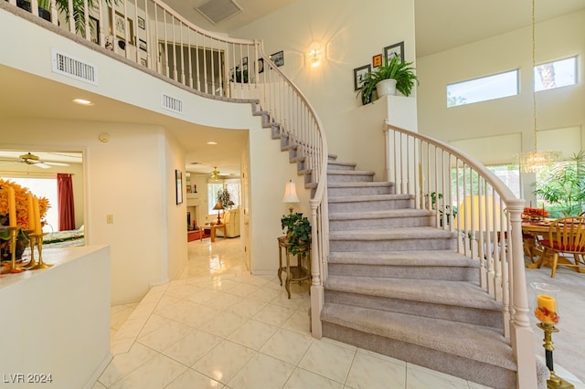 stairway featuring ceiling fan with notable chandelier, tile patterned floors, and a towering ceiling