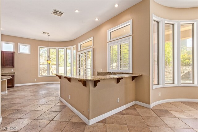 kitchen with a kitchen breakfast bar, hanging light fixtures, kitchen peninsula, and light stone counters