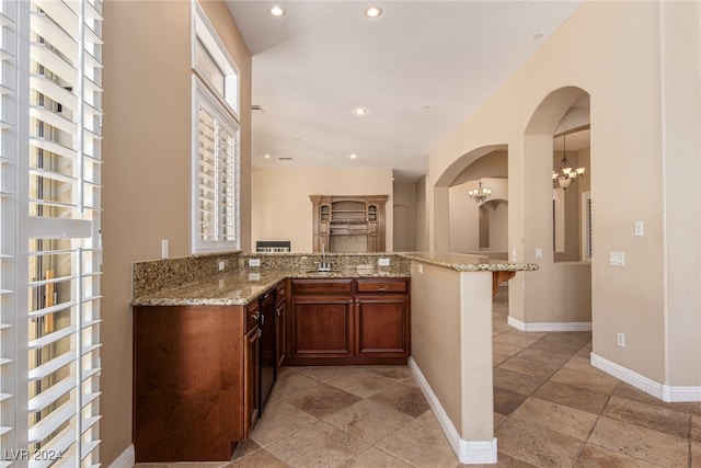 bar with light stone countertops, a chandelier, and sink