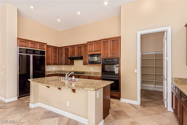 kitchen featuring a kitchen breakfast bar, a kitchen island with sink, black appliances, and light stone counters