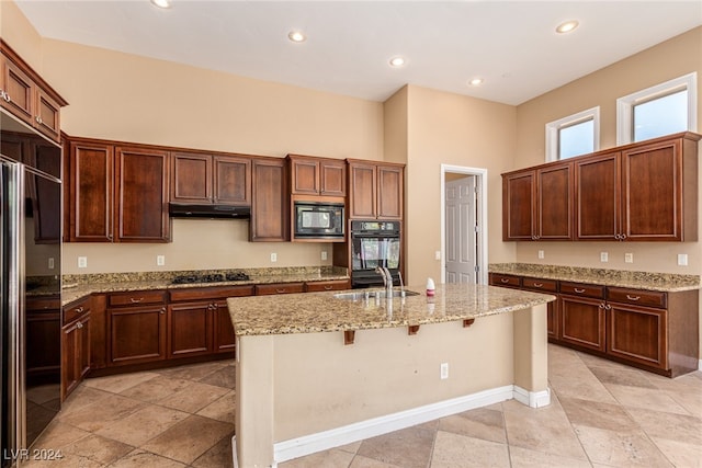 kitchen with black appliances, a kitchen bar, light stone countertops, sink, and an island with sink