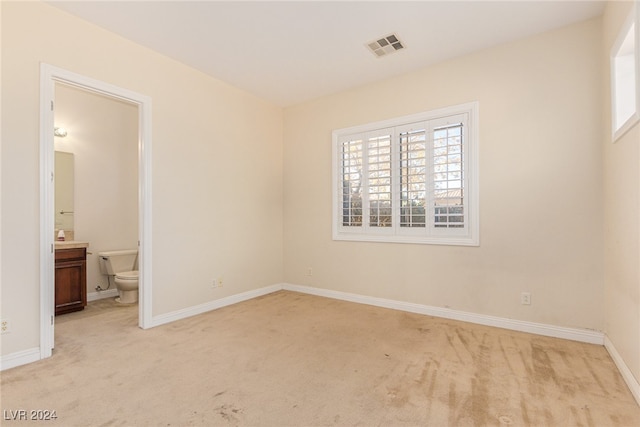 unfurnished bedroom with ensuite bathroom and light carpet