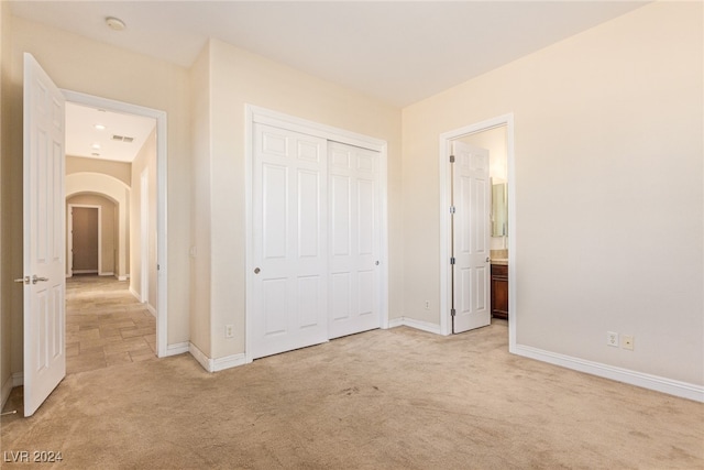 unfurnished bedroom with connected bathroom, a closet, and light colored carpet