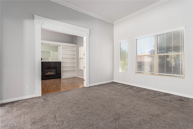 unfurnished living room featuring a tiled fireplace, built in features, dark carpet, and ornamental molding