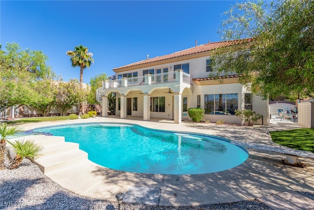 rear view of property featuring a patio, a balcony, and a fenced in pool