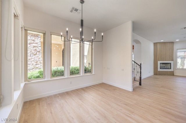 unfurnished dining area with a chandelier, a large fireplace, and light hardwood / wood-style flooring