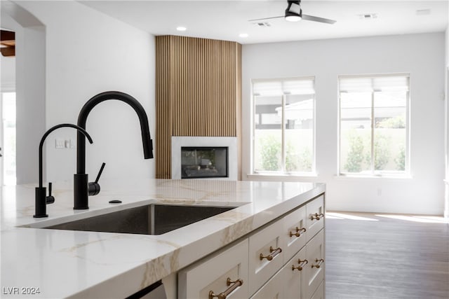 kitchen featuring hardwood / wood-style floors, white cabinets, sink, a large fireplace, and light stone counters