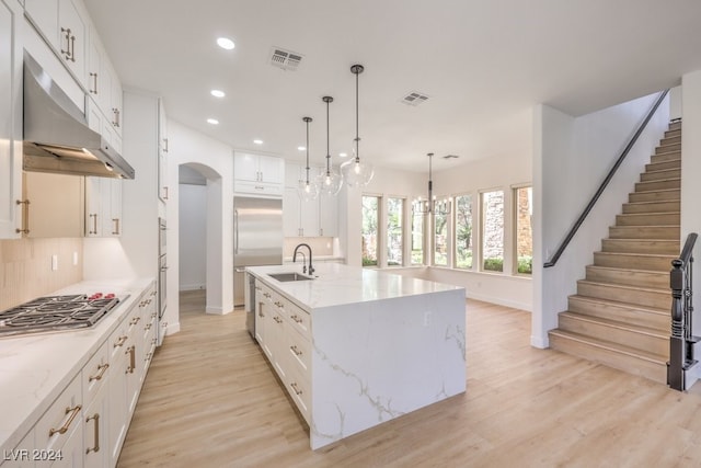 kitchen featuring appliances with stainless steel finishes, pendant lighting, light hardwood / wood-style flooring, white cabinetry, and a large island