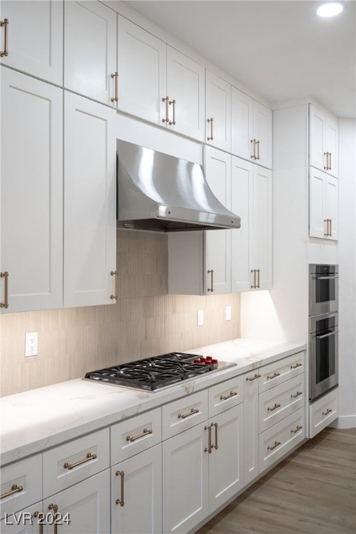 kitchen featuring ventilation hood, light hardwood / wood-style floors, white cabinetry, and stainless steel appliances