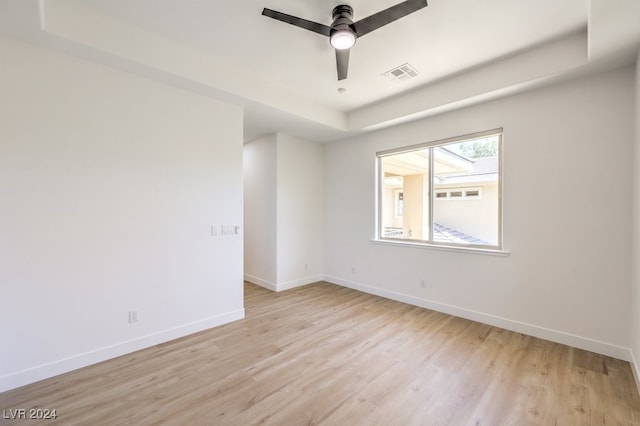 empty room featuring ceiling fan, a tray ceiling, and light hardwood / wood-style flooring