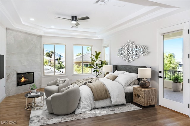 bedroom with dark wood-type flooring, a tile fireplace, ceiling fan, access to exterior, and a tray ceiling