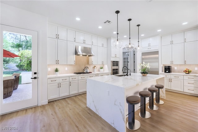 kitchen featuring ventilation hood, white cabinets, a kitchen island with sink, and appliances with stainless steel finishes