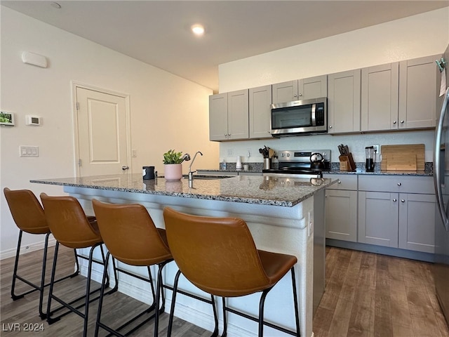 kitchen featuring dark wood-type flooring, sink, an island with sink, a breakfast bar, and appliances with stainless steel finishes