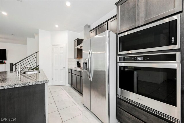 kitchen featuring light stone counters, backsplash, appliances with stainless steel finishes, light tile patterned floors, and sink