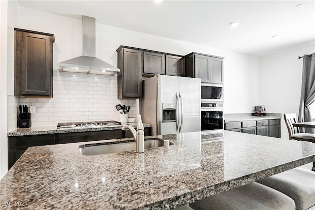 kitchen with sink, light stone counters, appliances with stainless steel finishes, tasteful backsplash, and wall chimney exhaust hood