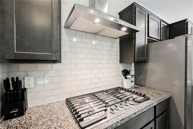 kitchen featuring light stone counters, decorative backsplash, wall chimney exhaust hood, and stainless steel gas stovetop