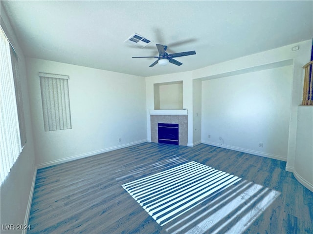 unfurnished living room featuring ceiling fan, dark wood-type flooring, and a tiled fireplace