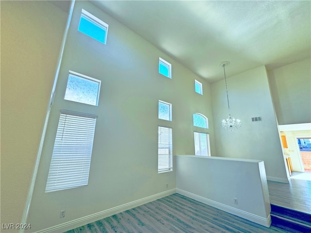 empty room with hardwood / wood-style flooring, a high ceiling, and an inviting chandelier