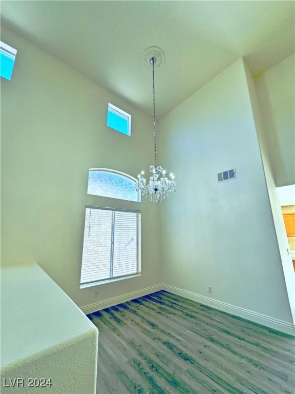 unfurnished dining area featuring a towering ceiling, a notable chandelier, and hardwood / wood-style flooring