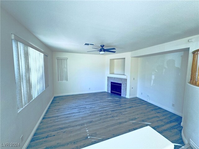 unfurnished living room with a textured ceiling, a tiled fireplace, ceiling fan, and dark hardwood / wood-style floors