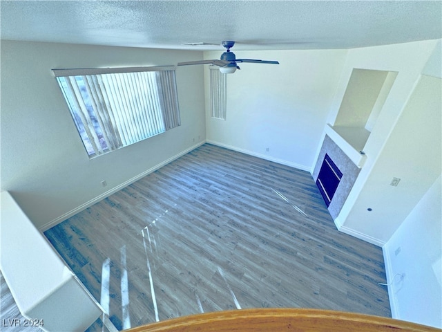 unfurnished living room with ceiling fan, a fireplace, dark hardwood / wood-style flooring, and a textured ceiling