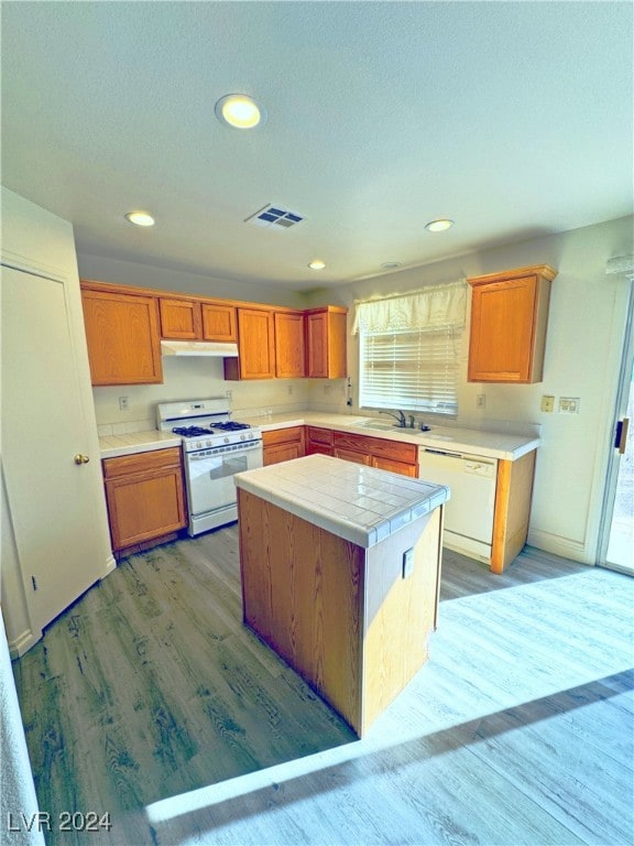 kitchen with white appliances, sink, wood-type flooring, a center island, and tile counters