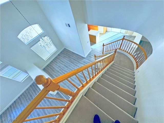 staircase with hardwood / wood-style floors, a high ceiling, and a chandelier