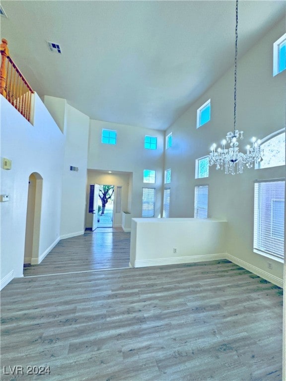 unfurnished living room featuring hardwood / wood-style floors, high vaulted ceiling, and a chandelier