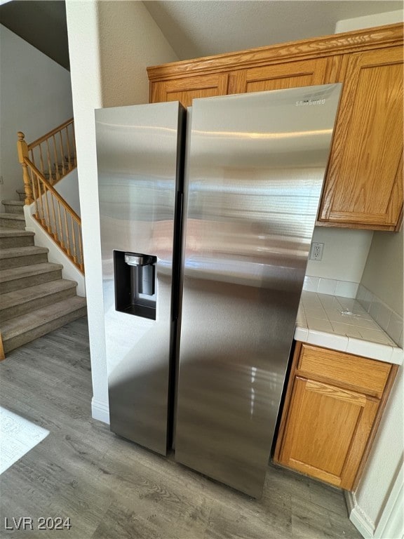 kitchen featuring stainless steel fridge with ice dispenser, tile counters, and light wood-type flooring