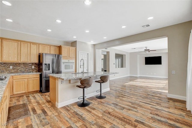 kitchen with a center island with sink, light stone counters, oven, stainless steel fridge with ice dispenser, and light hardwood / wood-style flooring