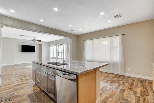 kitchen featuring light stone counters, sink, hardwood / wood-style flooring, stainless steel dishwasher, and a kitchen island with sink