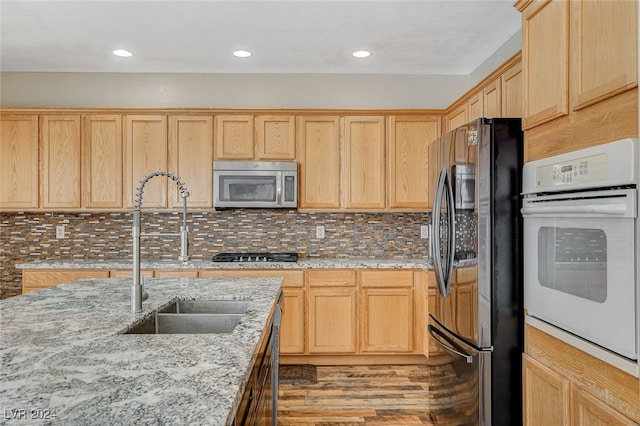 kitchen with tasteful backsplash, stainless steel appliances, light stone countertops, sink, and light hardwood / wood-style flooring