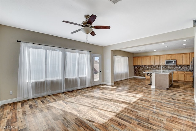 unfurnished living room with light hardwood / wood-style floors, ceiling fan, and sink