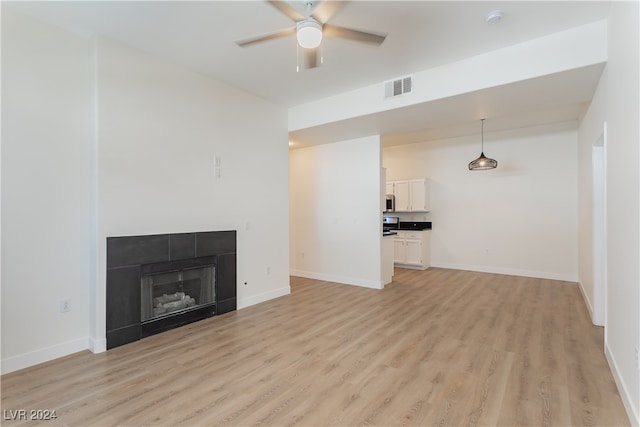 unfurnished living room with light wood-type flooring, ceiling fan, and a tile fireplace