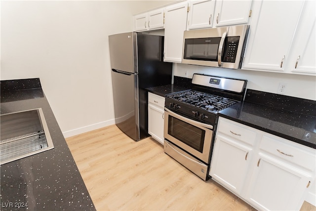 kitchen featuring white cabinets, light hardwood / wood-style floors, dark stone countertops, and appliances with stainless steel finishes