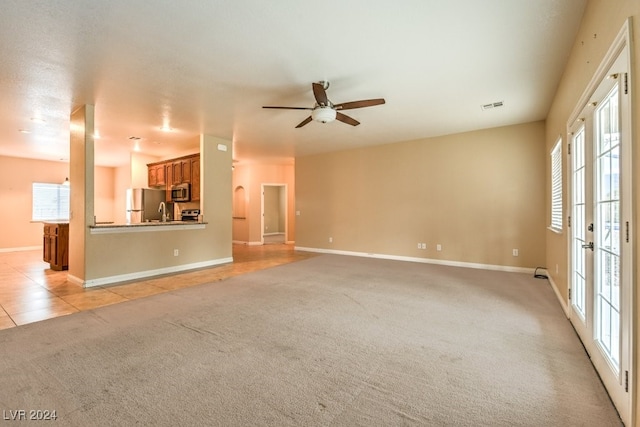 unfurnished living room with light colored carpet, a healthy amount of sunlight, and ceiling fan