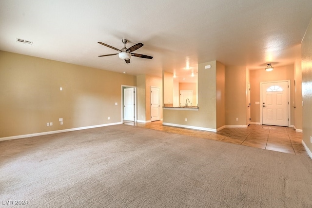 unfurnished living room featuring ceiling fan, a textured ceiling, light carpet, and sink