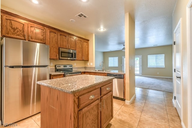 kitchen with a center island, a textured ceiling, sink, ceiling fan, and appliances with stainless steel finishes