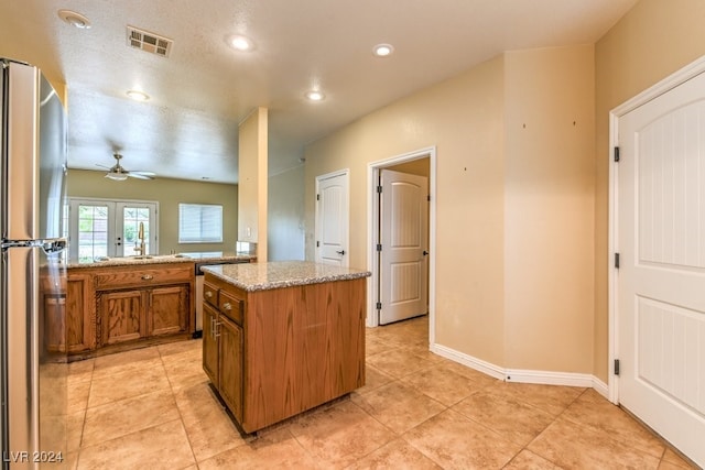 kitchen featuring light stone counters, ceiling fan, a center island, stainless steel fridge, and french doors